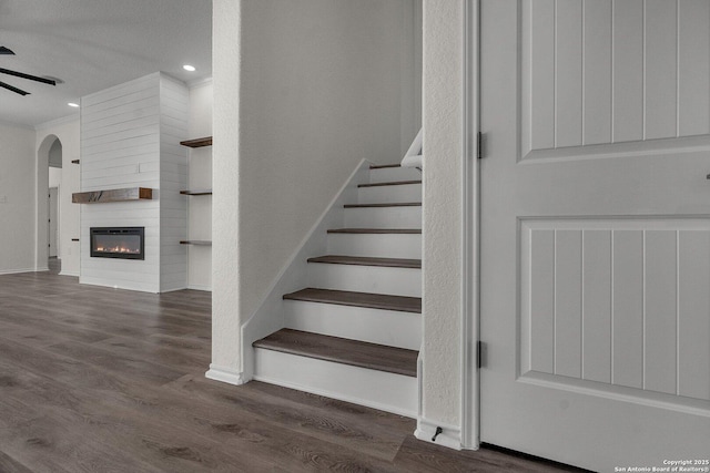 stairs with a large fireplace, baseboards, recessed lighting, wood finished floors, and arched walkways