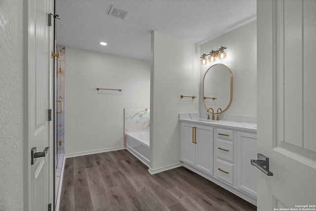 full bath featuring visible vents, vanity, a garden tub, wood finished floors, and a textured ceiling