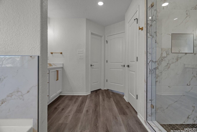 bathroom with a marble finish shower, vanity, a textured wall, and wood finished floors