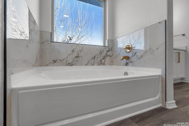 bathroom with a garden tub, wood finished floors, and a textured wall