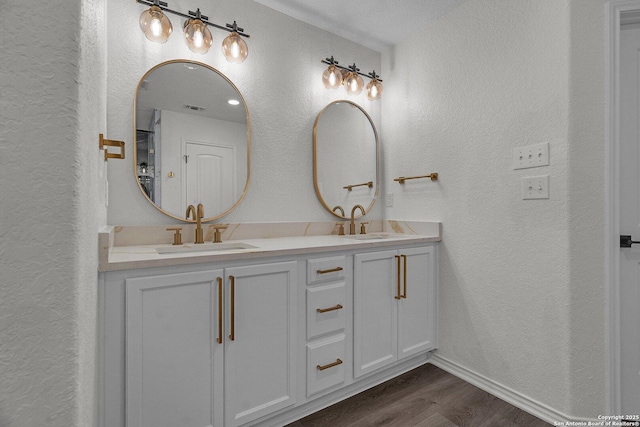 bathroom with a sink, wood finished floors, double vanity, and a textured wall