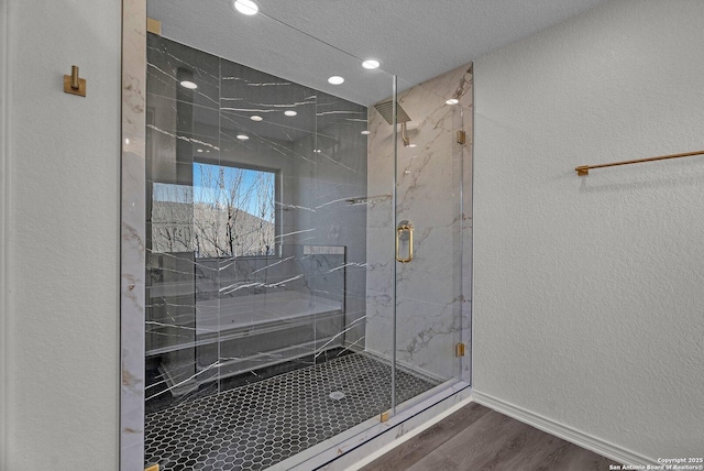 bathroom with wood finished floors, recessed lighting, a marble finish shower, baseboards, and a textured wall