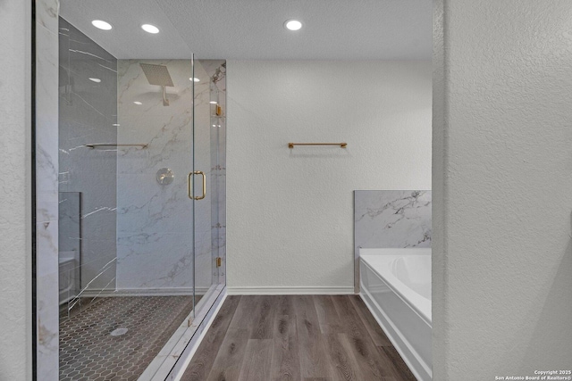 bathroom featuring wood finished floors, a marble finish shower, baseboards, a bath, and a textured wall