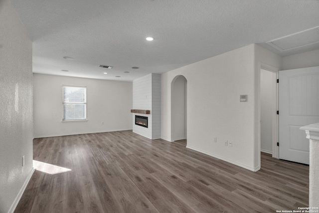 unfurnished living room featuring visible vents, a textured ceiling, wood finished floors, a large fireplace, and baseboards