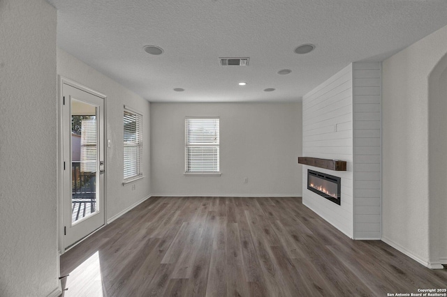 unfurnished living room featuring visible vents, a fireplace, a textured ceiling, and dark wood-type flooring