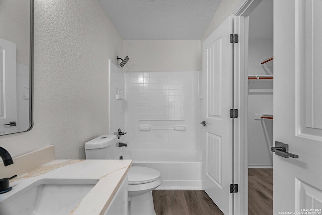 full bathroom featuring toilet, vanity, wood finished floors, a textured wall, and a textured ceiling