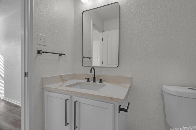 half bath featuring toilet, vanity, and a textured wall