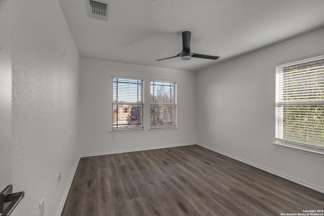 spare room featuring dark wood-style floors, visible vents, a wealth of natural light, and baseboards