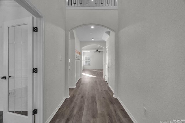 hall with arched walkways, baseboards, and dark wood-style flooring