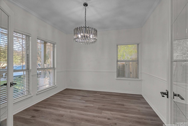 empty room with french doors, an inviting chandelier, wood finished floors, and crown molding