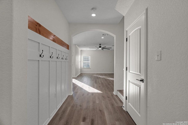 mudroom featuring baseboards, ceiling fan, dark wood finished floors, a textured wall, and arched walkways