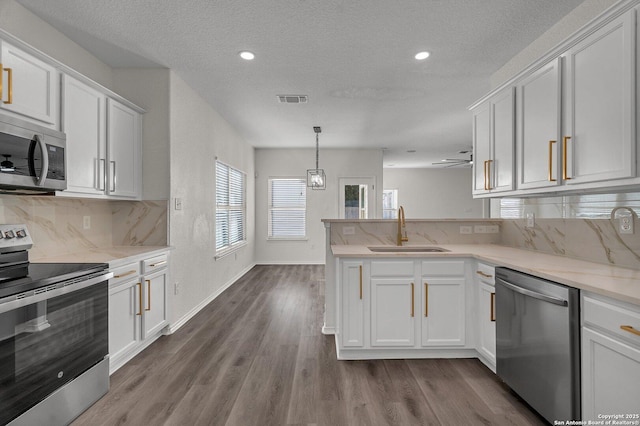 kitchen with visible vents, a peninsula, a sink, appliances with stainless steel finishes, and white cabinetry