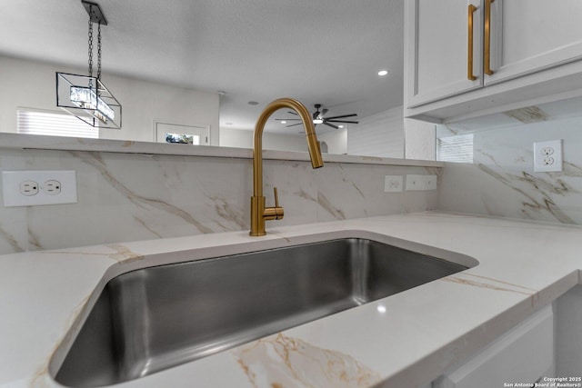 room details with a sink, decorative light fixtures, light stone counters, backsplash, and white cabinets