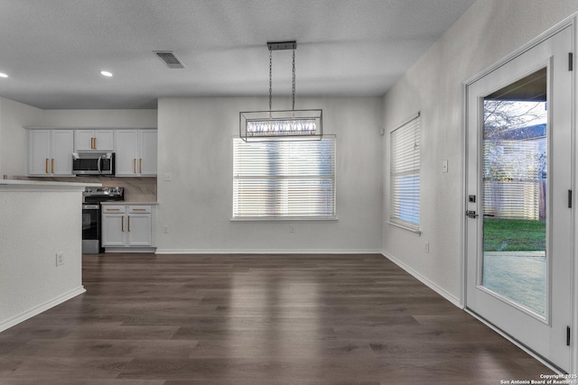 unfurnished dining area featuring dark wood finished floors, visible vents, a textured ceiling, and baseboards