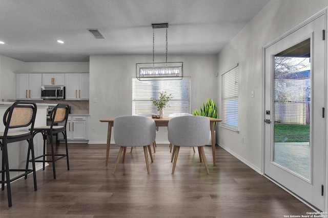 dining space featuring dark wood-style floors, visible vents, a textured ceiling, and baseboards