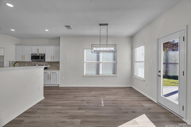 kitchen featuring stainless steel microwave, wood finished floors, visible vents, and white cabinets