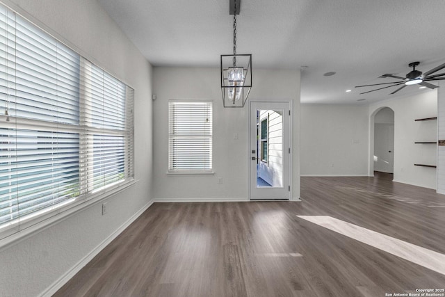 interior space with arched walkways, a ceiling fan, baseboards, and wood finished floors