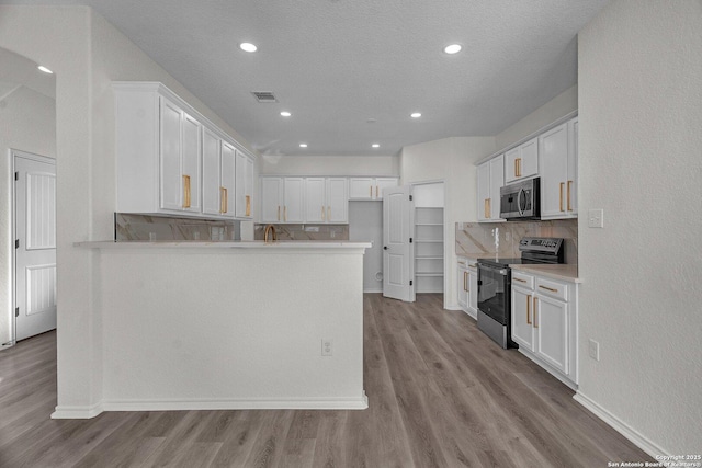 kitchen with visible vents, light wood-style flooring, backsplash, stainless steel appliances, and a peninsula