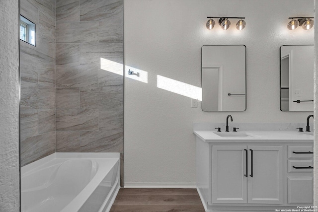 full bath featuring a sink, wood finished floors, double vanity, baseboards, and a bathtub