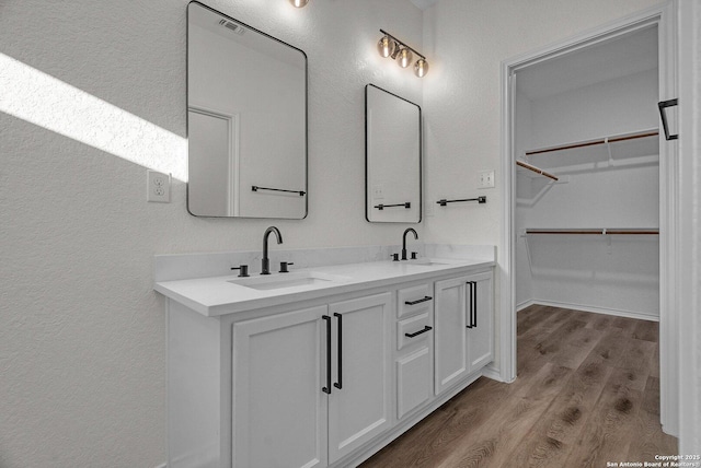 full bath featuring double vanity, a spacious closet, wood finished floors, and a sink