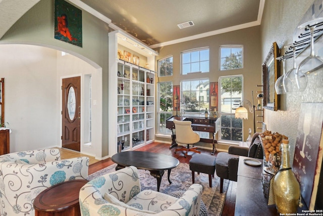 sitting room featuring visible vents, wood finished floors, arched walkways, crown molding, and a towering ceiling