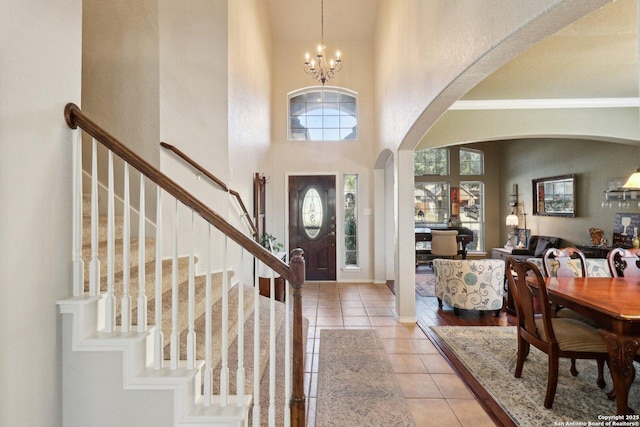 tiled entrance foyer with an inviting chandelier, stairway, arched walkways, and a towering ceiling