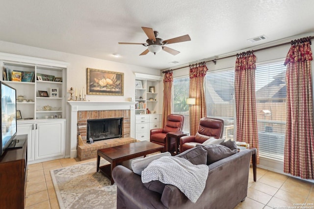 living room featuring a ceiling fan, a textured ceiling, light tile patterned flooring, and a fireplace