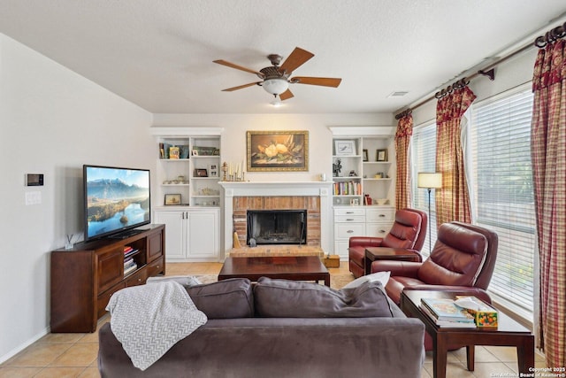 living room featuring visible vents, ceiling fan, a fireplace, light tile patterned flooring, and a textured ceiling