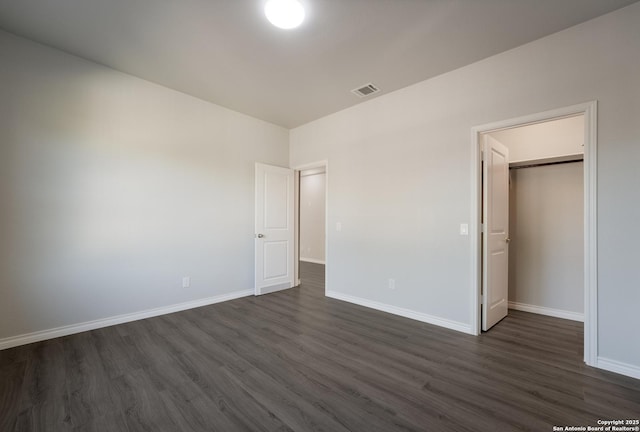 unfurnished bedroom featuring visible vents, baseboards, dark wood-type flooring, and a spacious closet