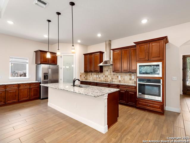kitchen with tasteful backsplash, visible vents, light wood-type flooring, stainless steel appliances, and wall chimney exhaust hood