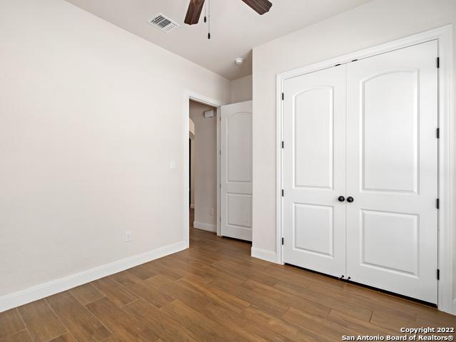 unfurnished bedroom featuring wood finished floors, visible vents, baseboards, ceiling fan, and a closet