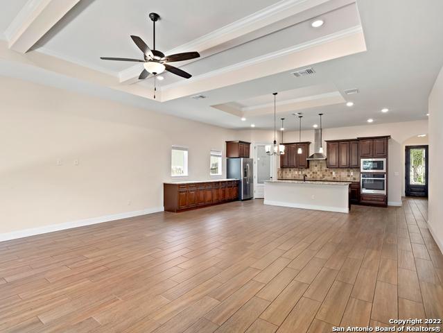 unfurnished living room with visible vents, a raised ceiling, ceiling fan with notable chandelier, and light wood finished floors