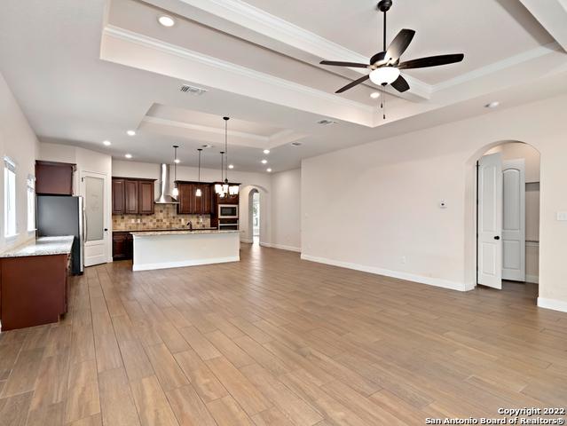 unfurnished living room with a raised ceiling, light wood-style flooring, arched walkways, and ceiling fan