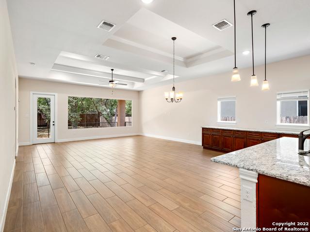 kitchen featuring light wood finished floors, visible vents, ceiling fan with notable chandelier, and a raised ceiling