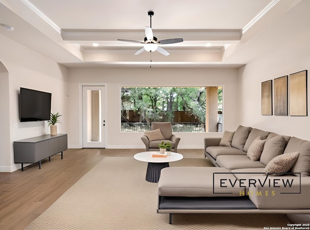 living room with a tray ceiling, wood finished floors, baseboards, and ornamental molding