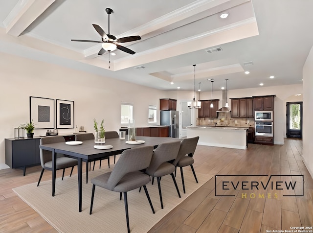 dining room featuring a tray ceiling, light wood-style floors, visible vents, and crown molding