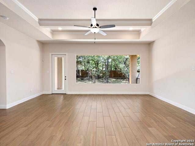 interior space with arched walkways, a raised ceiling, wood finished floors, and crown molding