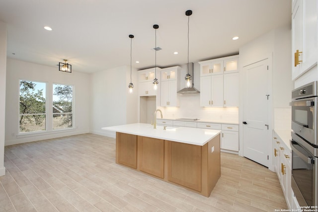 kitchen featuring black electric cooktop, a sink, wall chimney range hood, light countertops, and decorative backsplash