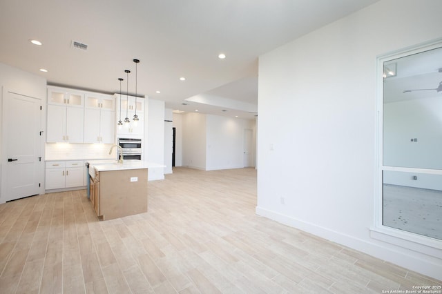 kitchen with tasteful backsplash, open floor plan, a center island with sink, light wood-type flooring, and light countertops