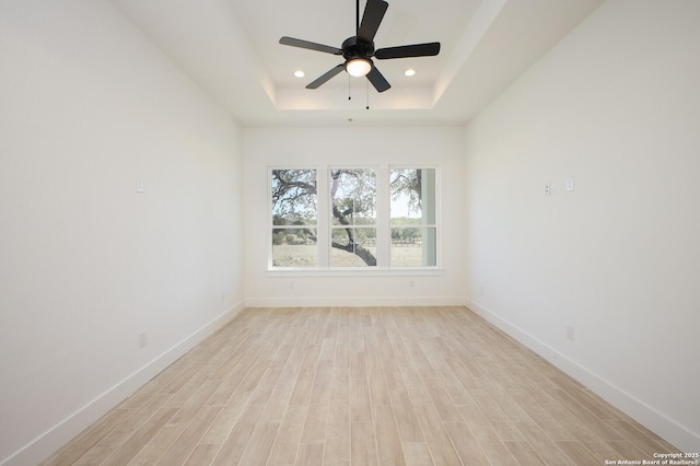 unfurnished room featuring a tray ceiling, recessed lighting, light wood-style floors, and baseboards