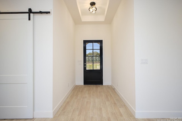 entryway with light wood-style flooring, baseboards, a tray ceiling, and a barn door