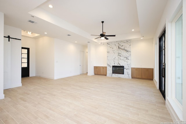 unfurnished living room with a barn door, a raised ceiling, visible vents, and a high end fireplace