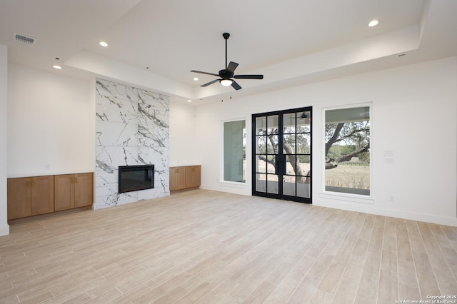 unfurnished living room with recessed lighting, a tray ceiling, a high end fireplace, and light wood finished floors