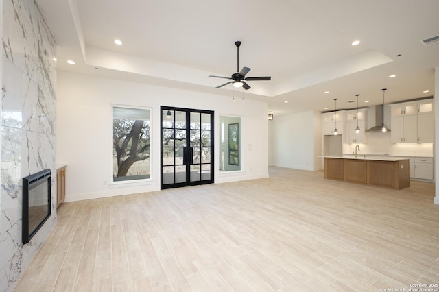 unfurnished living room with a fireplace, a raised ceiling, and light wood-style floors