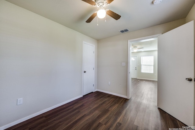 spare room with dark wood-style floors, visible vents, a ceiling fan, and baseboards