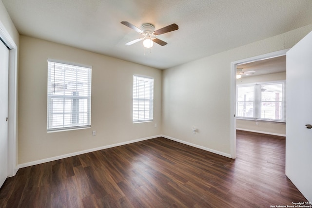 empty room with a wealth of natural light, baseboards, ceiling fan, and dark wood-style flooring