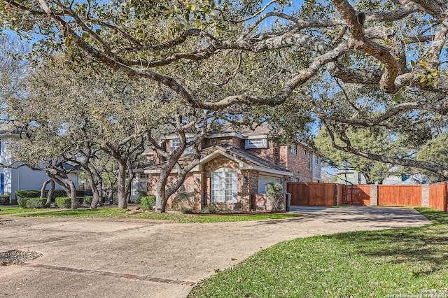 view of front of home with a front yard, brick siding, driveway, and fence