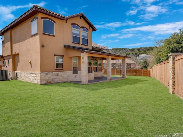 back of house with stucco siding, a fenced backyard, a yard, a patio area, and stone siding