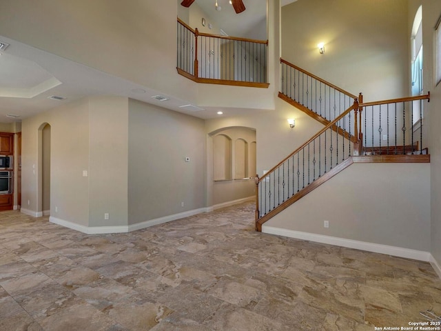 unfurnished living room featuring ceiling fan, stairs, baseboards, and a towering ceiling