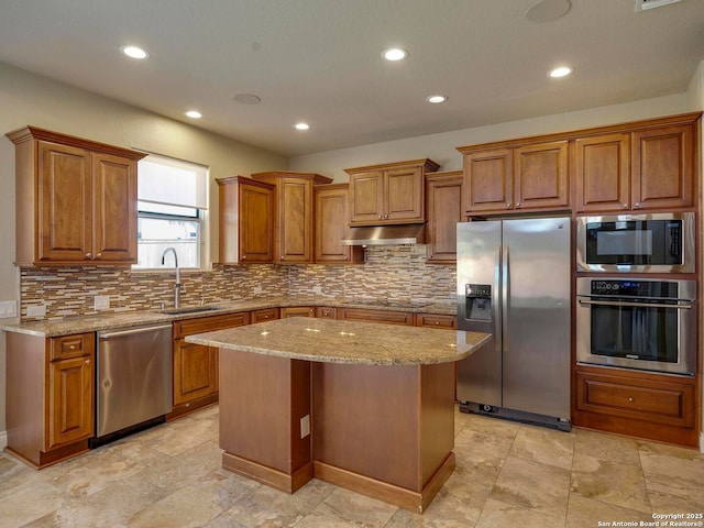 kitchen featuring under cabinet range hood, a sink, stainless steel appliances, brown cabinetry, and decorative backsplash